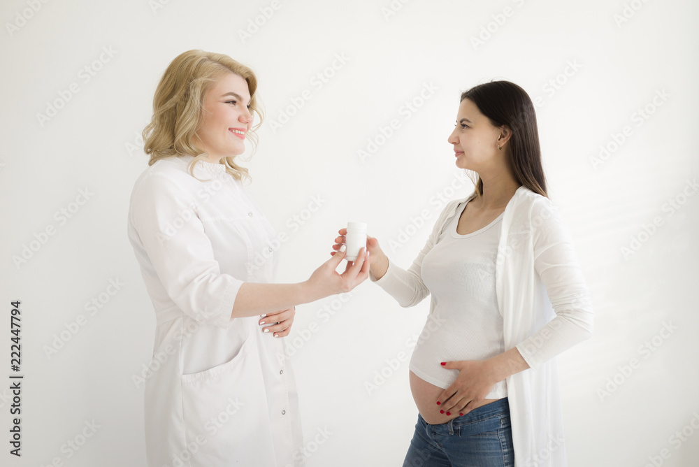 Pregnant girl at the doctor's reception. The doctor passes the jar of vitamins (medicines, tablets) to the pregnant woman. Pregnant girl at the doctor's reception. The doctor passes the jar of vitamins (medicines, tablets) to the pregnant woman.