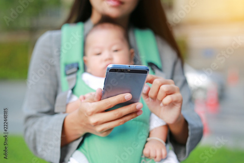 Close-up business mother in suit is using smartphone with carrying her baby boy in hipseat. Mother working with Baby. 