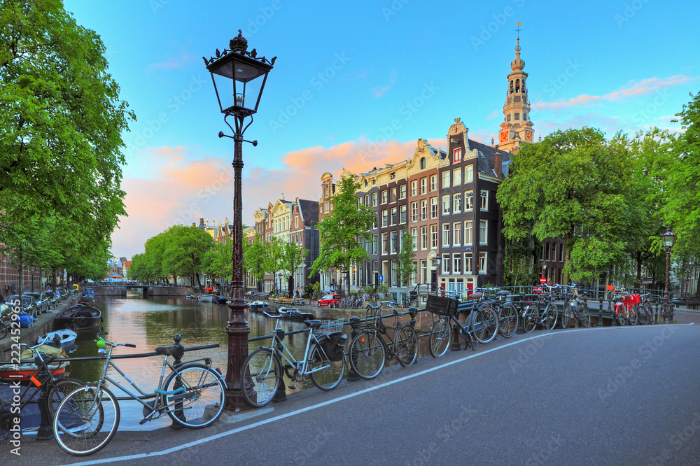 Fototapeta premium Pejzaż Amsterdamu o zachodzie słońca z uliczną latarnią przy słynnym kanale Kloveniersburgwal i południowym kościele w Holandii