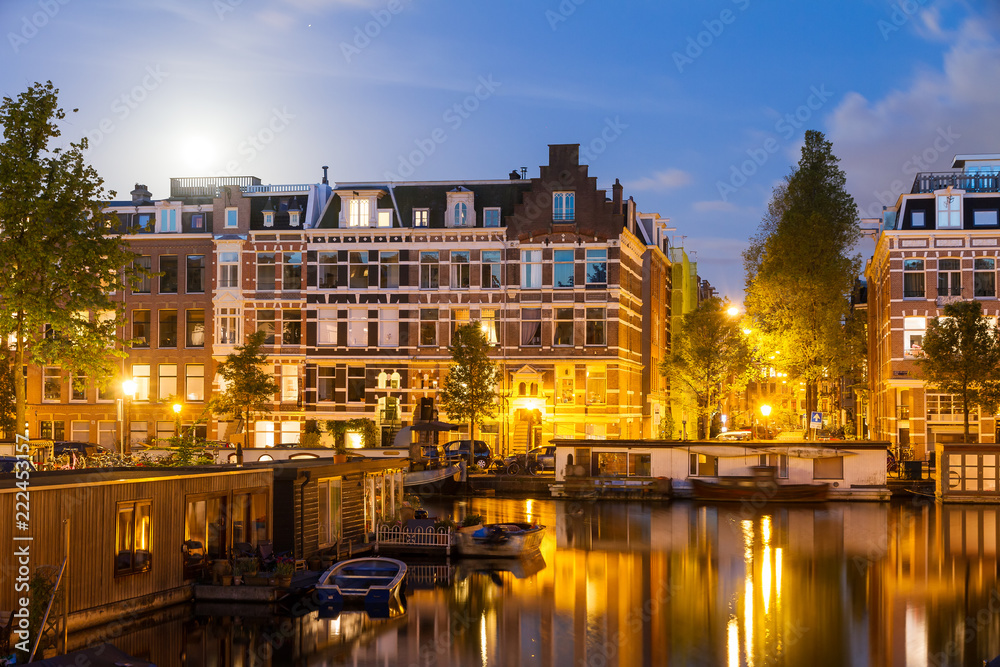 Beautiful cityscape of the famous canals of Amsterdam, the Netherlands, at night with a mirror reflection and a full moon