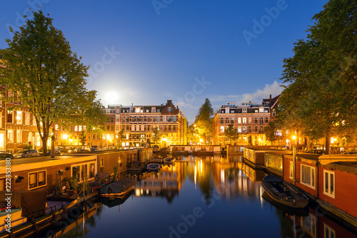 Beautiful cityscape of the famous canals of Amsterdam, the Netherlands, at night with a mirror reflection and houseboats 