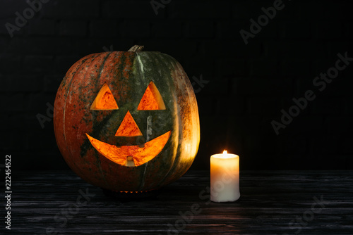 spooky halloween carved pumpkin with candle on wooden table on black background