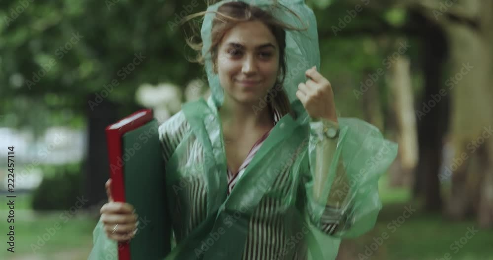 Rain day on the parc running young female holding some maps and wearing raincoat.