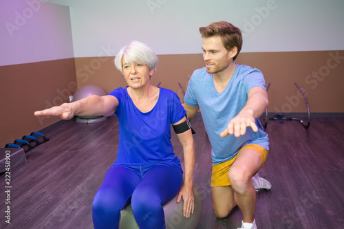 senior woman exercising assisted by a young male trainer