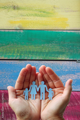 Paper family in hands on wooden coloured background welfare concept