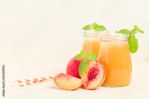 Peach smoothie in glass jars with fresh ripe fruits and green mint leaves on yellow pastel background.