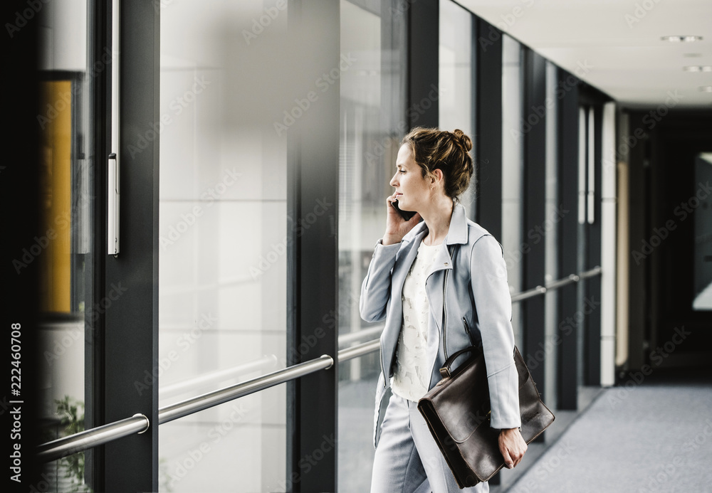 Businesswoman on cell phone looking out of window in office passageway Businesswoman on cell phone looking out of window in office passageway