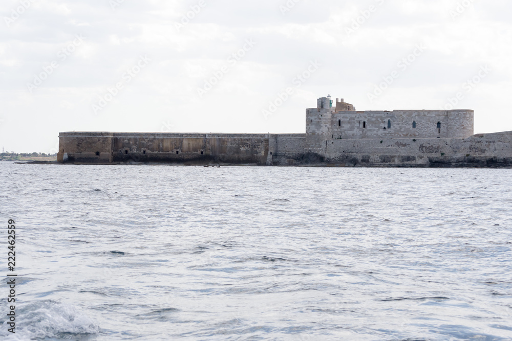 The gorgeous seafront of the island of Ortigia, in the city of Siracuse, Sicily(Italy). In this shot taken from a boat you can see the old city walls and the Maniace castle built in the 13th century.