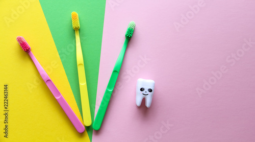 Plastic colorful toothbrushes and smiling tooth on a yellow, green, pink background. Dental care concept. Teeth care minimalism concept. photo