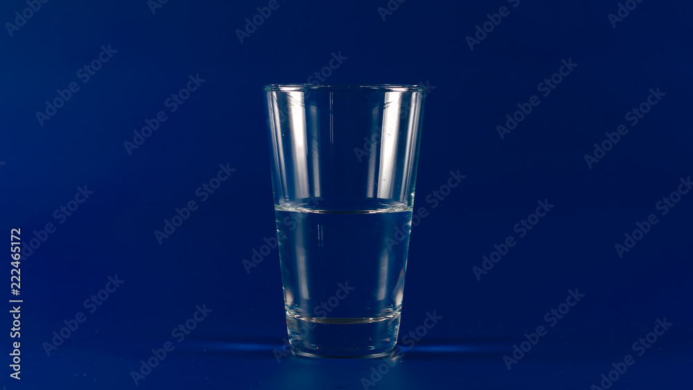 Glass with half of clear water on a blue background Glass with half of clear water on a blue background