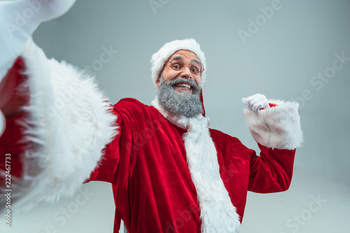 Funny guy with christmas hat posing at studio. New Year Holiday. Christmas, x-mas, winter, gifts concept. Man wearing Santa Claus costume on gray. Copy space. Winter sales.