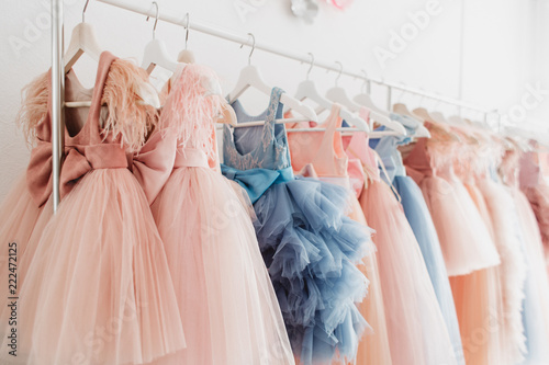 Foto Beautiful dressy lush pink and blue dresses for girls on hangers at the background of white wall