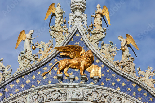 San Marco golden winged Lion statue with angels on basilica facade, symbol of Venice in a sunny day in Italy