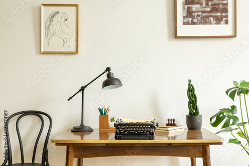 Framed drawing on a white wall above an antique, wooden desk with a vintage, black typewriter in a home office interior