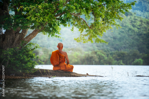 Buddhist monk in meditation beside the river with beautiful nature background