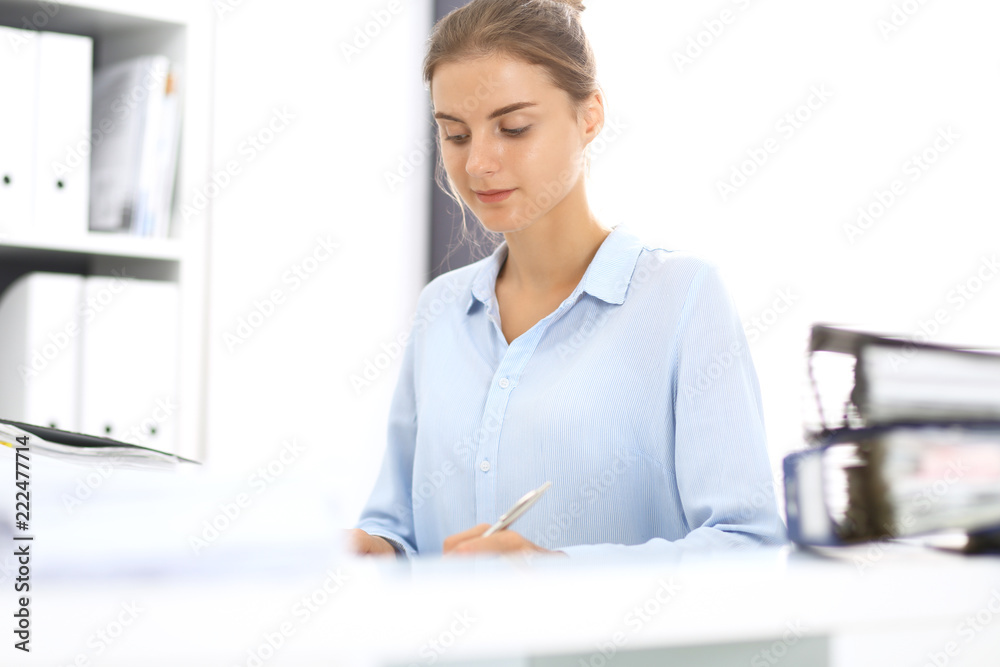 Woman bookkeeper or financial inspector calculating or checking balance, making report. Internal Revenue Service at work with financial document. Tax and audit concept Woman bookkeeper or financial inspector calculating or checking balance, making report. Internal Revenue Service at work with financial document. Tax and audit concept