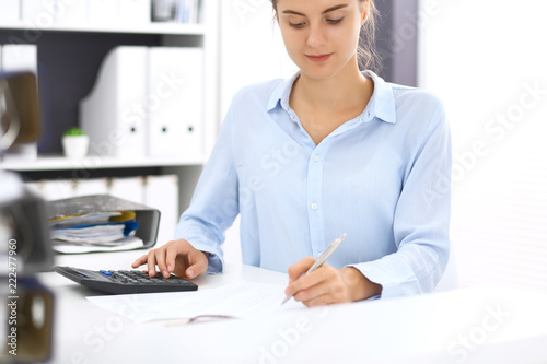 Woman bookkeeper or financial inspector calculating or checking balance, making report. Internal Revenue Service at work with financial document. Tax and audit concept