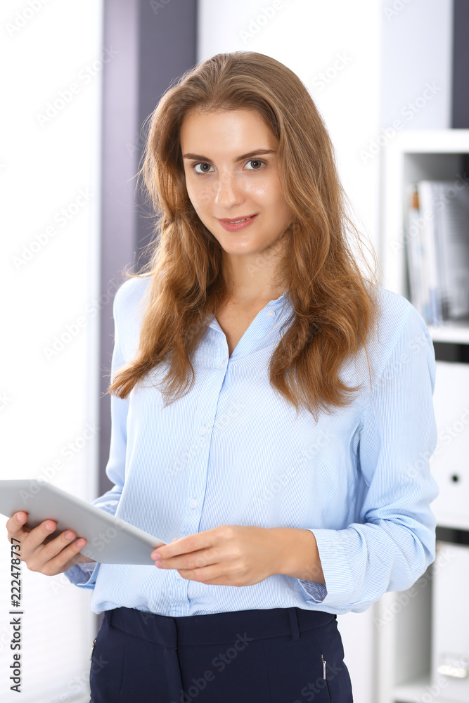 Young brunette business woman looks like a student girl at work in office. Girl standing straight with tablet pc Young brunette business woman looks like a student girl at work in office. Girl standing straight with tablet pc