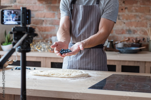 social media influencer or food blogger creating content. man shooting a cooking video using camera on tripod. chef holding bluberries in hands and showing them to viewer. photo