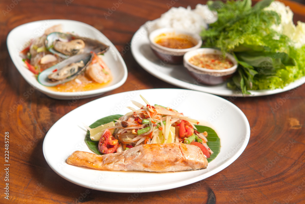 Grilled salmon steak, spicy Thai papaya salad  in white dish on wooden table background