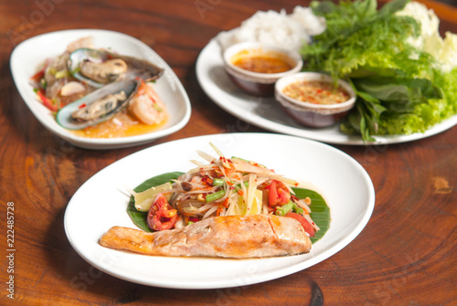 Grilled salmon steak, spicy Thai papaya salad in white dish on wooden table background