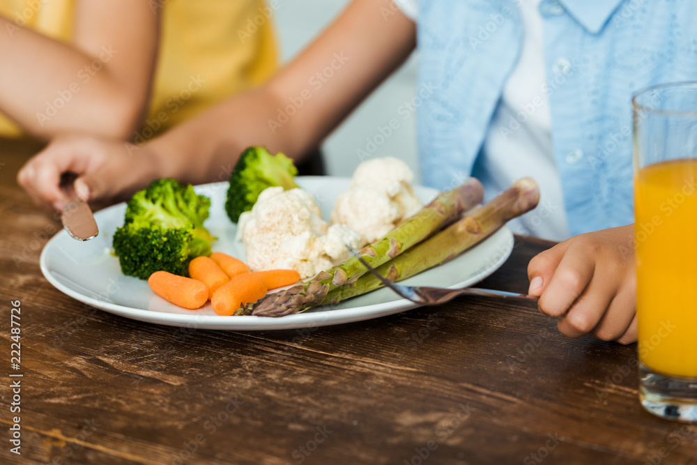 close-up partial view of child holding fork and knife while eating healthy vegetables