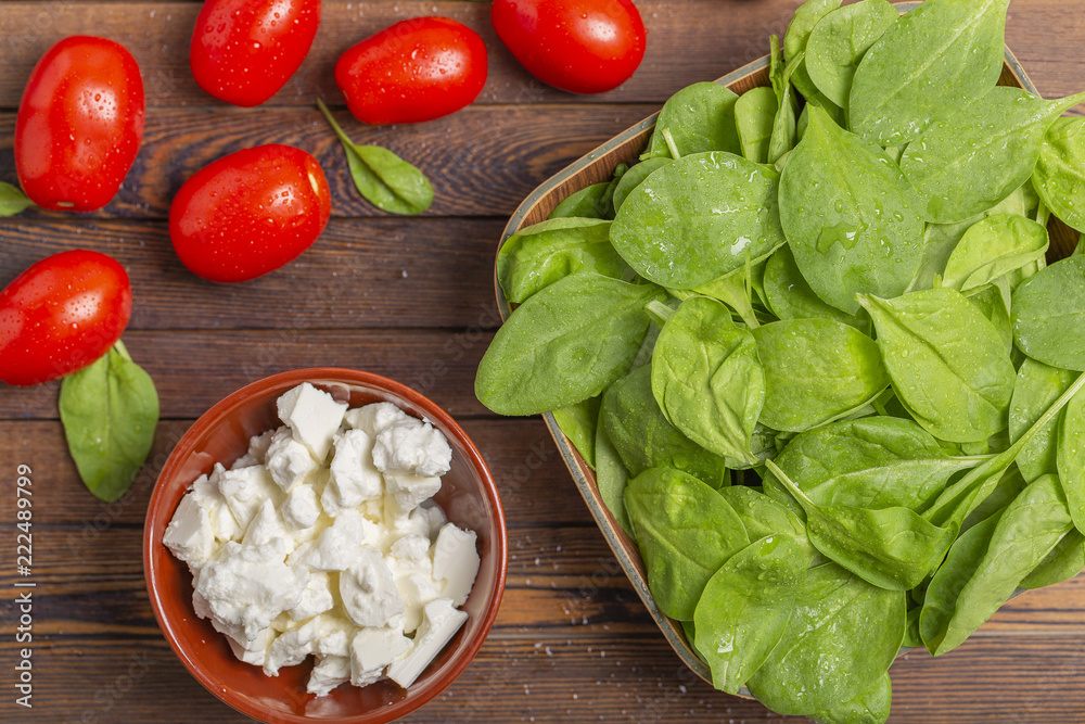 Fresh spinach leaves, feta cheese, tomatoes and spices on a dark wooden table Fresh spinach leaves, feta cheese, tomatoes and spices on a dark wooden table