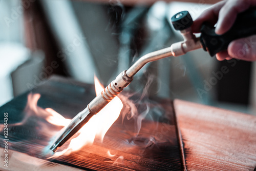 Fotografie Artisan and carpenter burning wood planks, focus on the gas burner pistol, made of brass and orange rubber cable