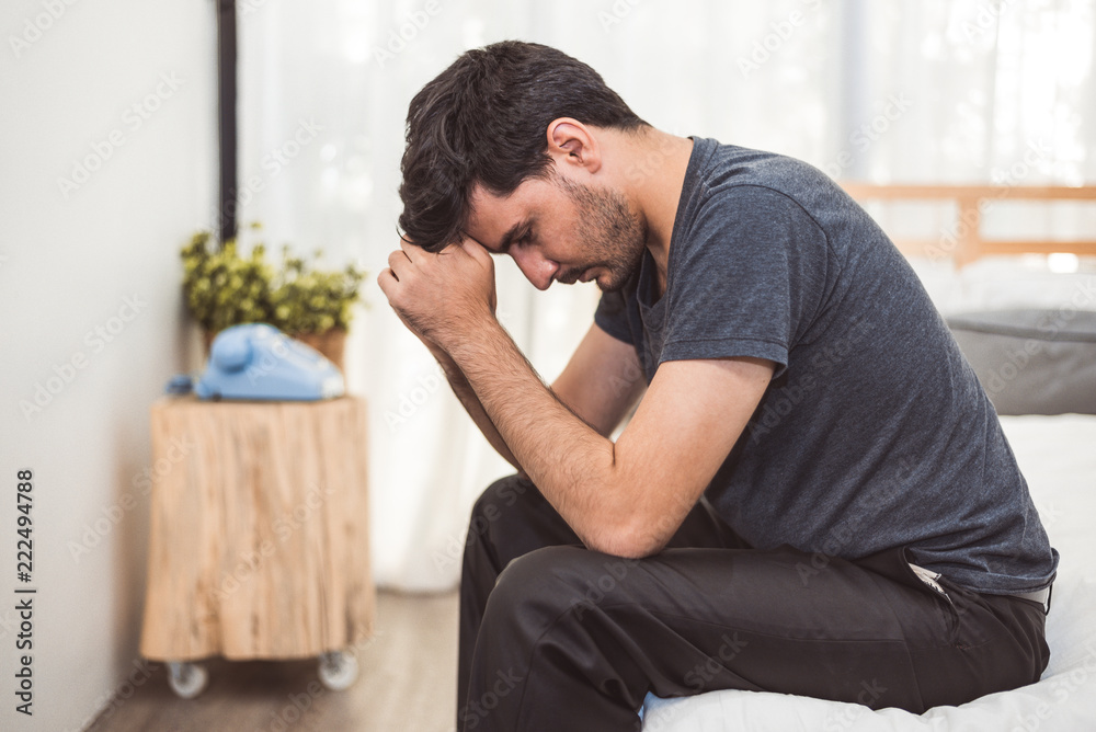 Worried man sitting on bed with hand on forehead in bedroom in serious mood emotion. Major Depressive Disorder called MDD concept. Lonely symptom of men alertness. Physical healthcare and social issue Worried man sitting on bed with hand on forehead in bedroom in serious mood emotion. Major Depressive Disorder called MDD concept. Lonely symptom of men alertness. Physical healthcare and social issue