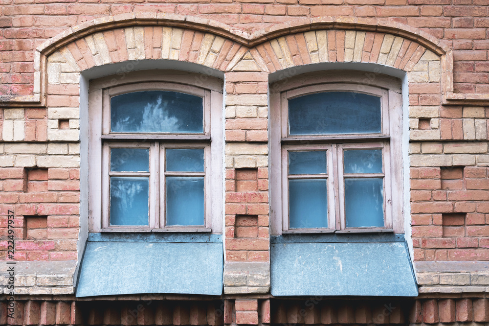 Two vintage arched windows in a wall of yellow bricks. Green - the colors of sea wave glass in a maroon dark red wooden frame. The concept of antique vintage architecture in building elements