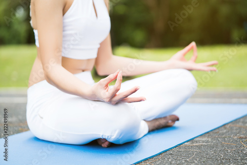 Young Woman wear white sportswear. Being meditated on yoga is in the garden. Make good health. Close up of beautiful hands. copy space