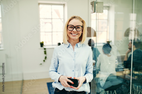 Smiling young businesswoman holding her cellphone in an office © Flamingo Images