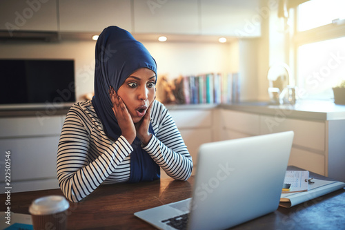Surprised looking Arabic female entrepreneur working online at h
