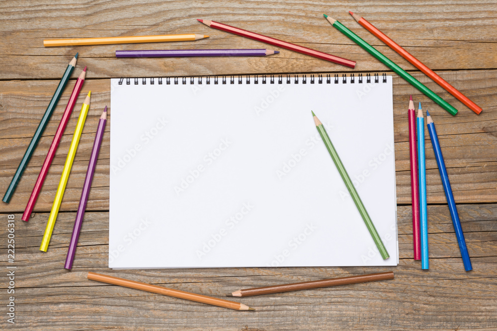 Blank page of a sketchbook with colored pencils on an old wooden table Blank page of a sketchbook with colored pencils on an old wooden table