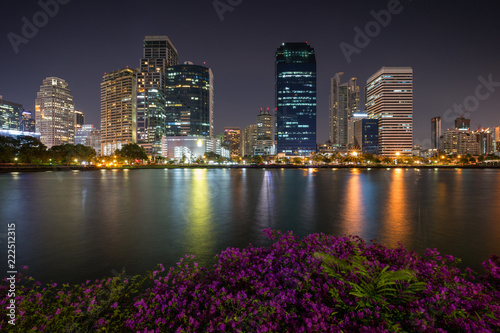 Scenic view of flowerbeds and lake at the Benjakiti (Benjakitti) Park and lit skyscrapers in Bangkok, Thailand, in the evening. © tuomaslehtinen