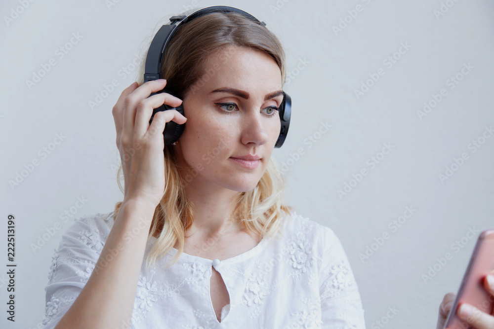 Beautiful blond girl with headphones on a light background. She enjoys listening to music and having fun Beautiful blond girl with headphones on a light background. She enjoys listening to music and having fun