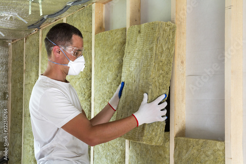 Quadro su tela Worker in protective goggles and respirator insulating rock wool insulation in wooden frame for future house walls for cold barrier