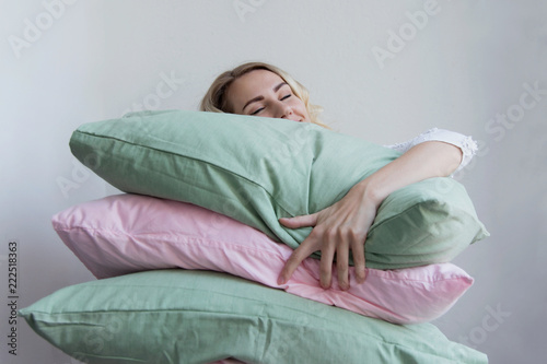 Beautiful blonde girl holds a lot of pillows in her hands. She lies on them with pleasure