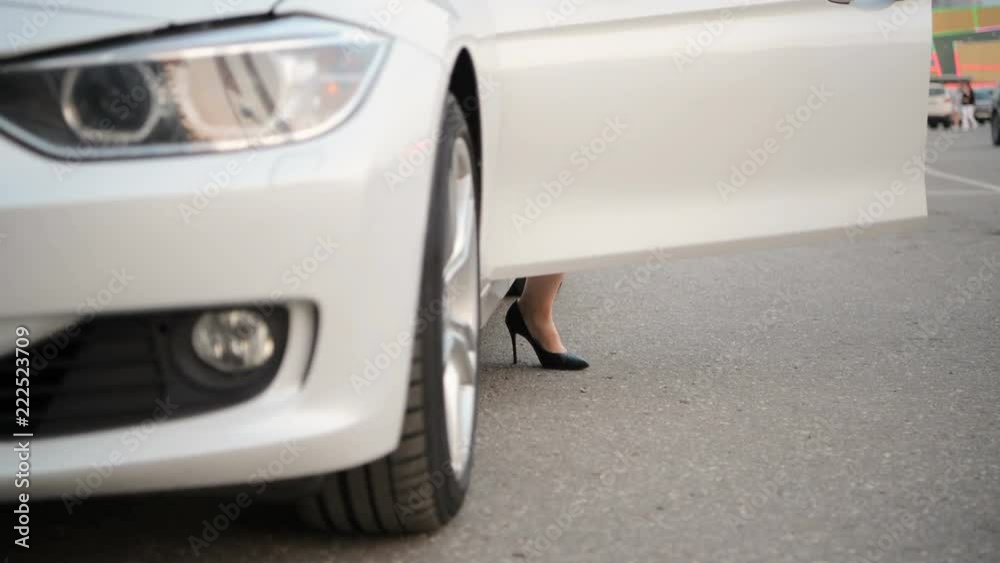 Women's heels come out of an expensive car and closes the doors of a car. Woman legs in high heels at the car in the city, urban. Women's heels come out of an expensive car and closes the doors of a car. Woman legs in high heels at the car in the city, urban.