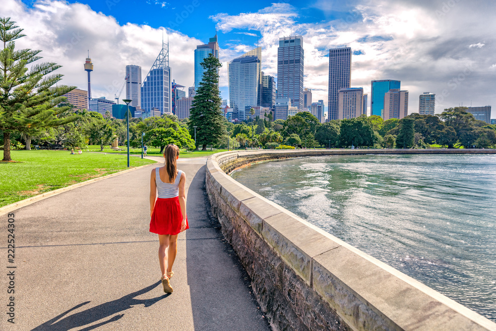 Naklejka premium Dziewczyna turystyczny Sydney city spaceru w parku miejskim z panoramą wieżowców w tle. Australia podróżuje wakacje latem. Styl życia Australijczyków.