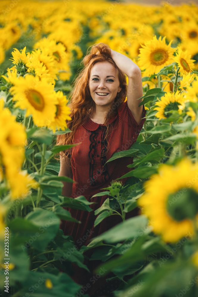 Young beautiful woman in a dress among blooming sunflowers. Agroculture.