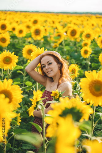 Young beautiful woman in a dress among blooming sunflowers. Agroculture.