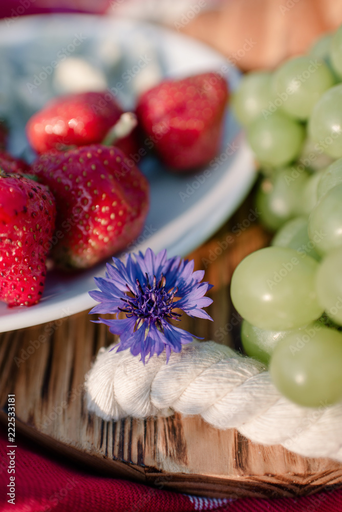 Composition on a picnic of grapes, strawberries and a flower on a wooden board