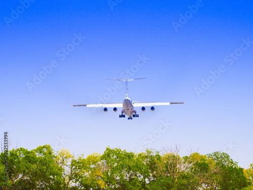 Small plane landing on airport. Propeller plane flies against a blue sky with white clouds and green trees
