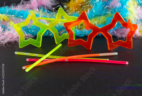 Neon Party supplies and Colorful Feather Boas on black background - colored led party lights - Photo booth Props. Copy Space. Party background