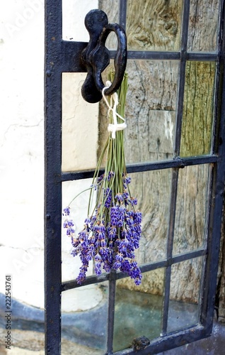 Fototapeta Naklejka Na Ścianę i Meble -  A sprig of lavender hung upside down to dry on the handle of a window outside a traditional medieval style house