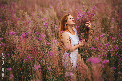 Beautiful red-haired girl in a dress in a flowering field of willow-tea.