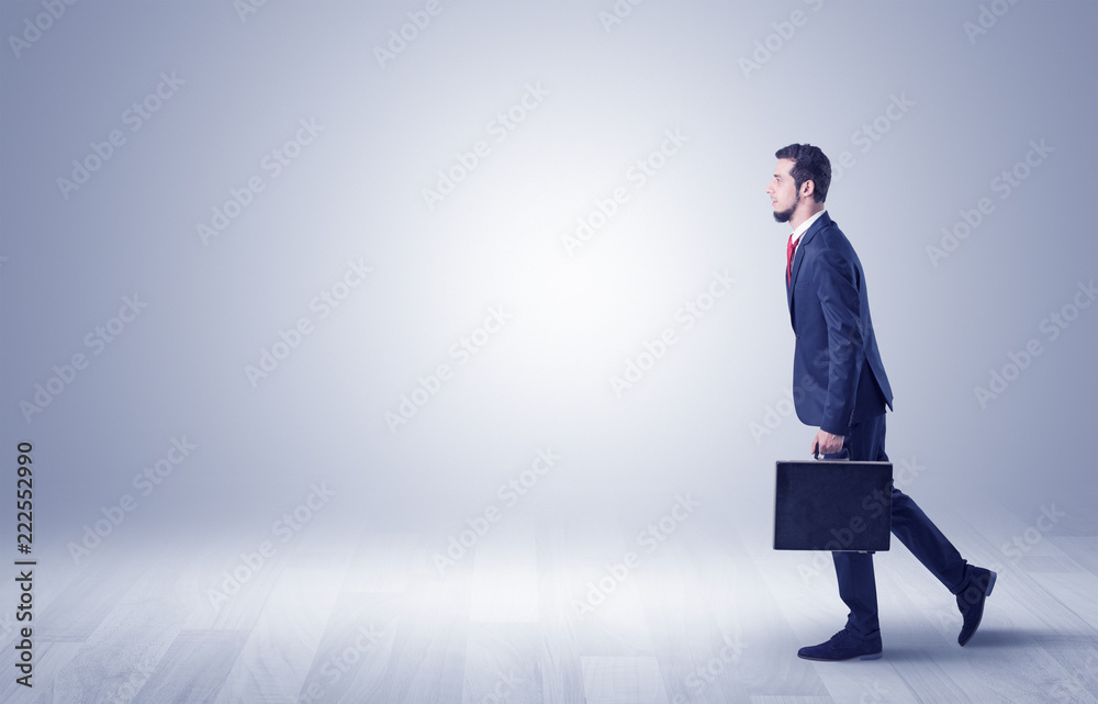 Successful businessman walking in front of an empty wall with briefcase on his hand
Successful businessman walking in front of an empty wall with briefcase on his hand