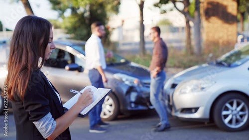 Car accident scene with wrecked car and Insurance person inspects the damage on a car and makes notes.