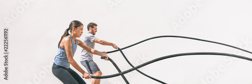 Gym fitness sport fit couple working out battle rope exercise banner panorama. Woman and man cross training amrs muscles and cardio with battling rope. Core workout panoramic crop.